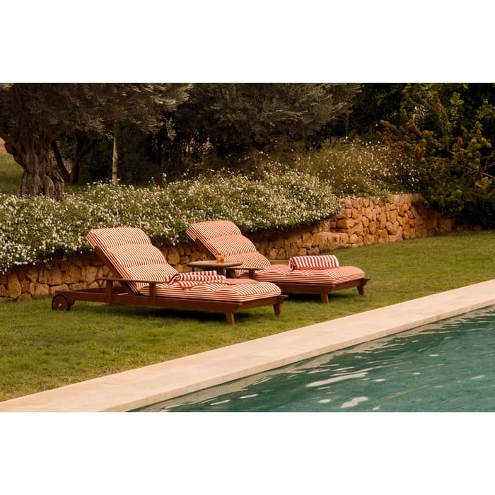 Two wooden lounge chairs with red and white striped cushions rest beside a pool, surrounded by lush greenery, stone walls, and mountain views in the background.