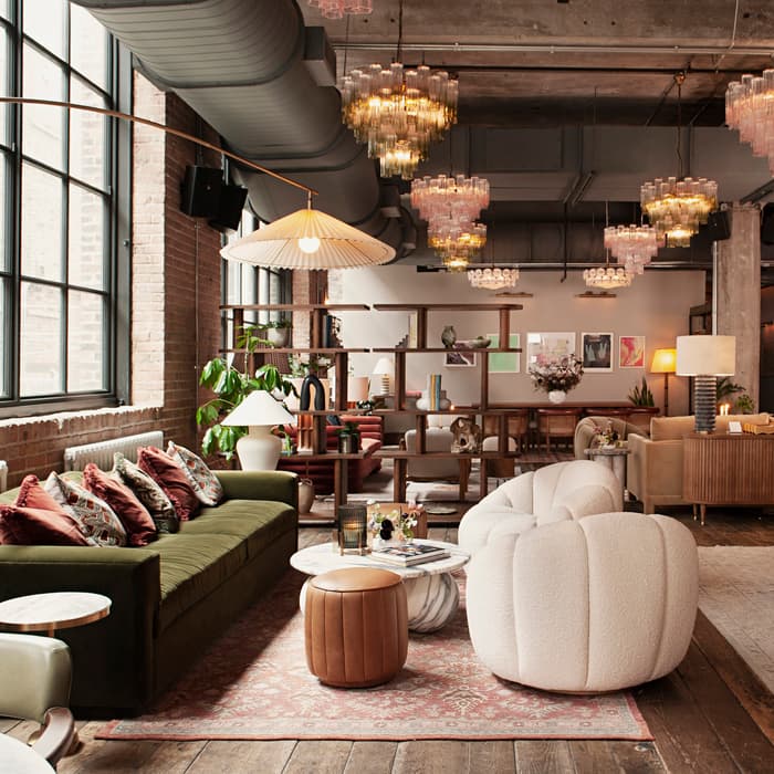 Cozy, industrial-style lounge displaying assorted seating options, modern fixtures, and decorative plants within a spacious, well-lit environment. Large windows and various light fixtures enhance the elegant ambience of the room.