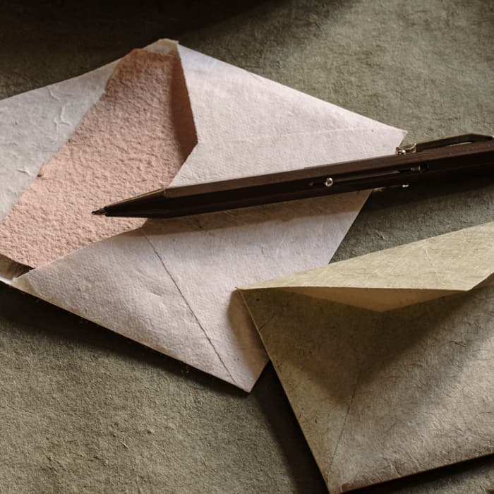 A metal plate with walnuts sits on a green cloth beside star anise, envelopes, a pen, and a red ribbon on a wooden table.