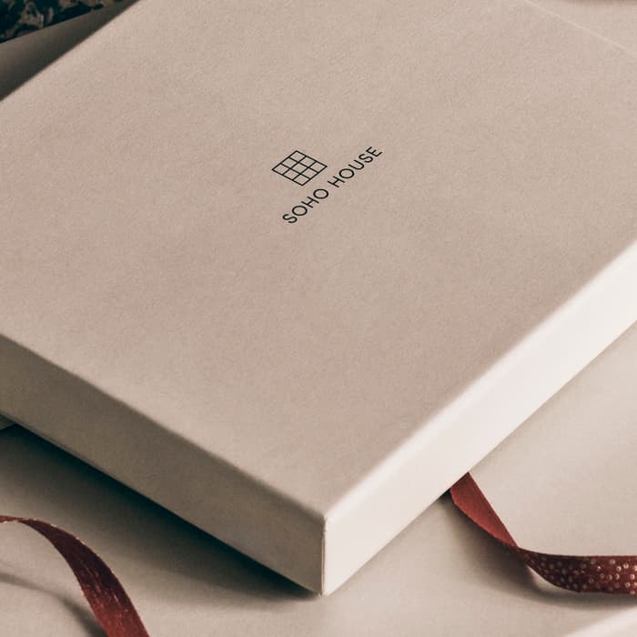 White gift boxes adorned with red ribbons are stacked with a "SONO HOUSE" label on the top box. A patterned wrapped gift with a red bow rests nearby on cloth.
