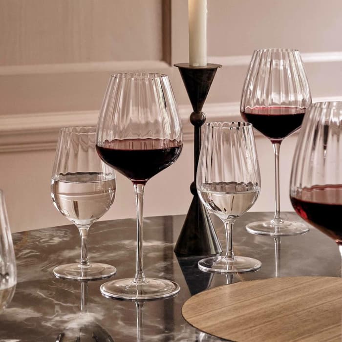 Wine glasses with red and clear liquids surround a lit candle on a dark marble table in an elegant, softly lit dining room.