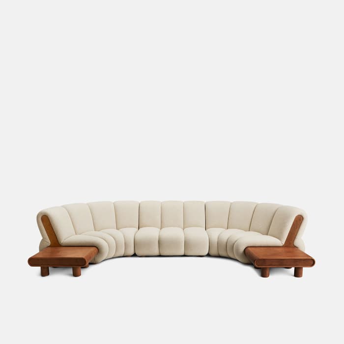 Curved beige sectional sofa with a plush, upholstered design, featuring wooden side tables integrated at both ends, set against a plain white background.