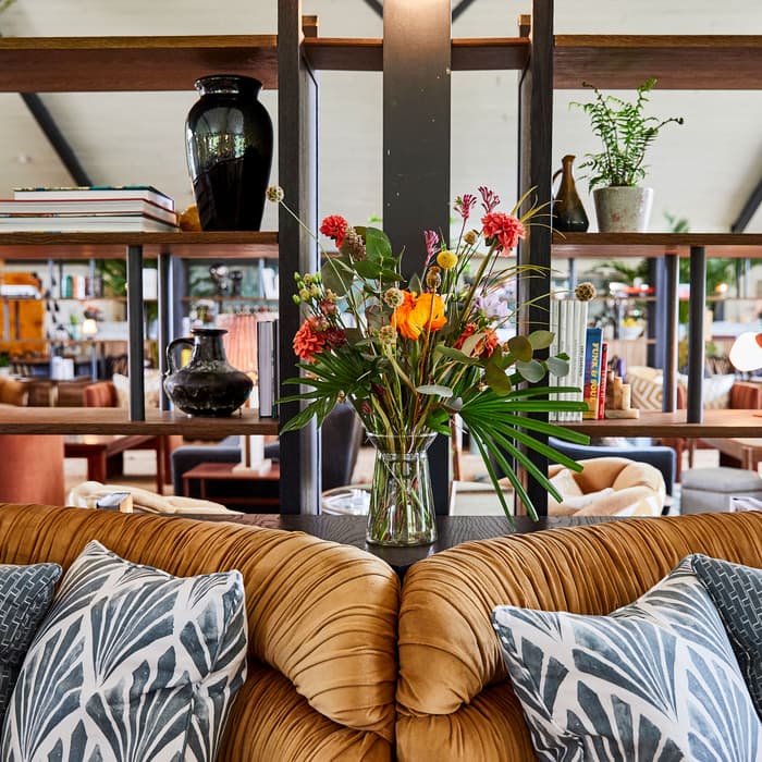 A vase with colorful flowers adorns a shelf. Surrounding objects include various books, vases, lamps, and plants. The background reveals a cozy, stylish, and well-decorated living space.