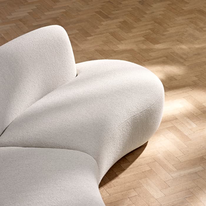 A curved, cream-colored couch sits on a wooden parquet floor, catching soft sunlight.