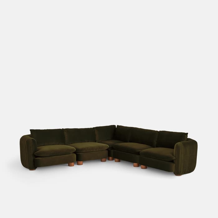 Green velvet sectional sofa with thick, cushioned seats and rounded armrests; it is set against a plain white background. The sofa has multiple seating sections, supported by wooden cylindrical legs.