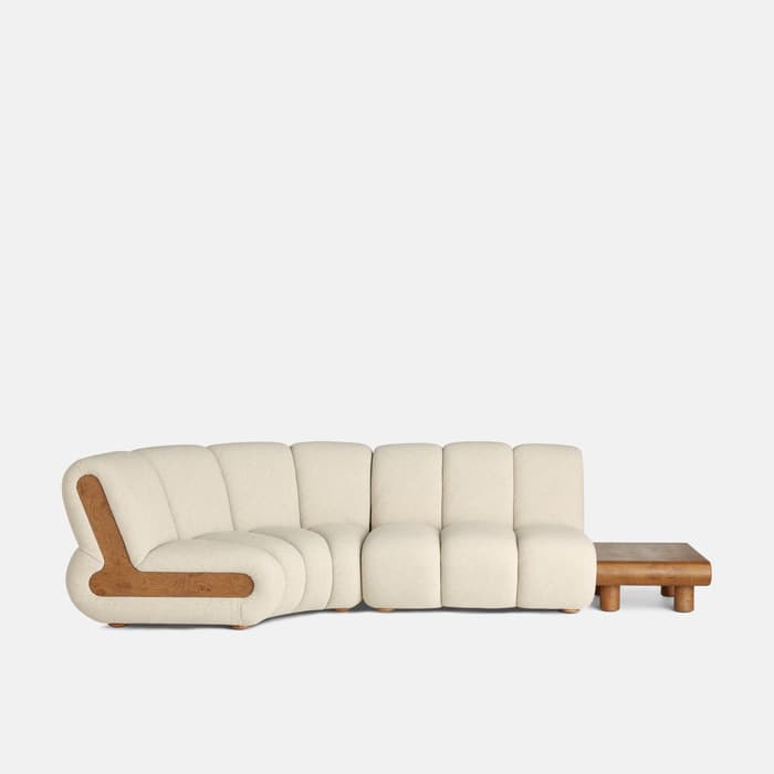 Curved, beige sectional sofa with wooden detailing, featuring plush seats and an integrated wooden coffee table on its right side, set against a plain, white background.