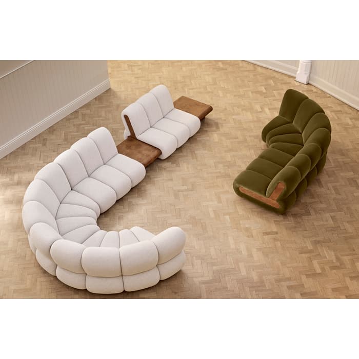 A cream modular sectional sofa with a wooden side table is positioned in a curved arrangement on a herringbone-patterned floor, facing an olive-green sofa in a minimalist room.