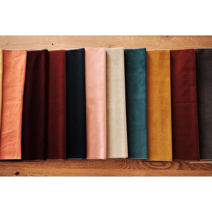 Folded fabric swatches are arranged in a row, showcasing different colors including peach, burgundy, beige, teal, mustard, and brown hues on a wooden surface.
