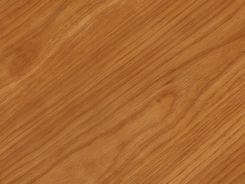 A rectangular wooden tabletop with a smooth, light brown surface partially extends over a white background, showing part of a leg in the bottom left corner.
