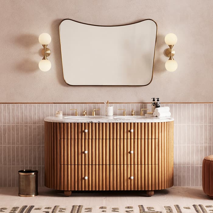Vanity with a wavy mirror and brass sconce lights stands against a tiled bathroom wall, featuring a wooden panelled cabinet, dual faucets, and countertop items like towels, soap, and toothbrushes.