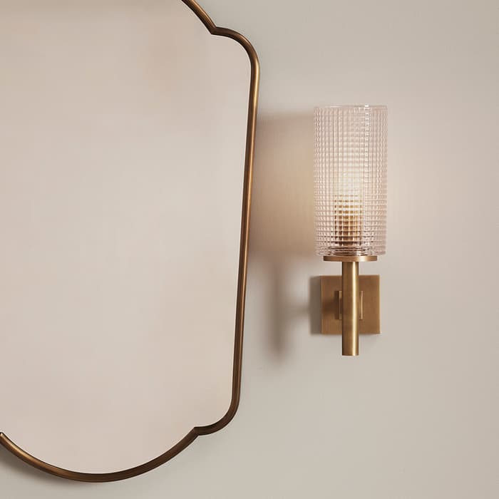 Marble bathroom sink with brass fixtures; soap, lotion, and hand wash on counter; brass-framed mirror and a brass sconce light fixture on a white wall. Text on bottles: "CowShed Hand Cream" and "CowShed Hand Wash".